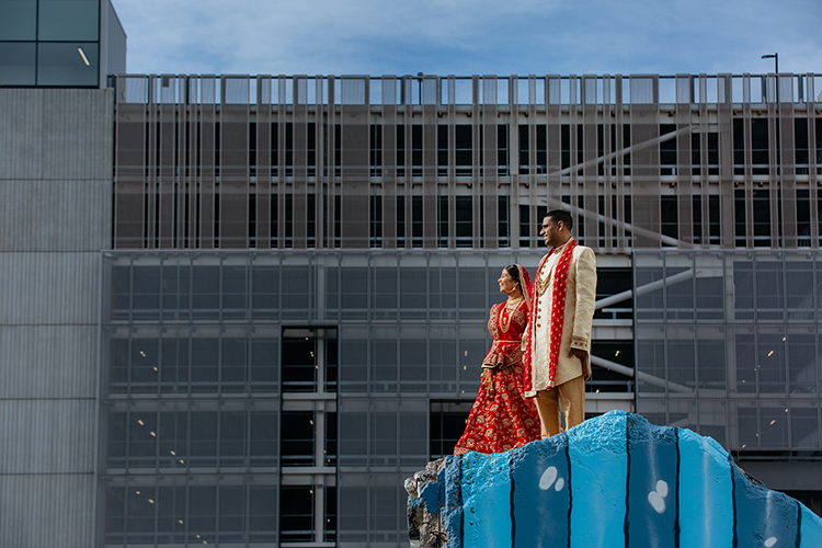 An Indian Bride and Groom standing on a earthquake ruin in Christchurch, New Zealand. They are wearing traditional Indian wedding attire and are standing side by side looking out in the same direction.