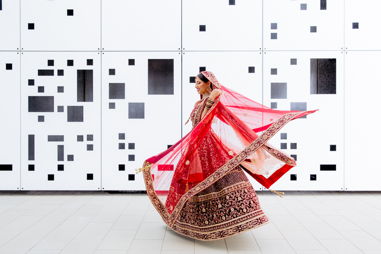 This is a photo from an Indian wedding in Auckland photographed by Mala Photography, and Auckland based wedding photographer that shoots Indian weddings throughout New Zealand. In this photo an Indian Bride dancing and spinning around in front of a white wall with black geometric shapes on it. 