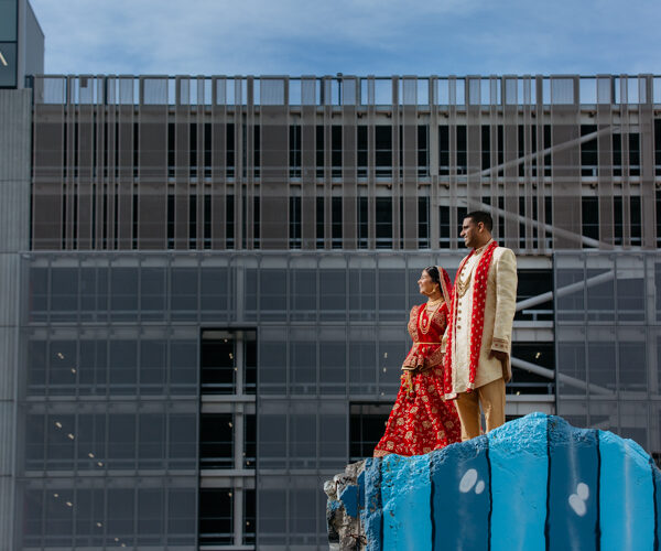 An Indian Bride and Groom standing on a earthquake ruin in Christchurch, New Zealand. They are wearing traditional Indian wedding attire and are standing side by side looking out in the same direction.